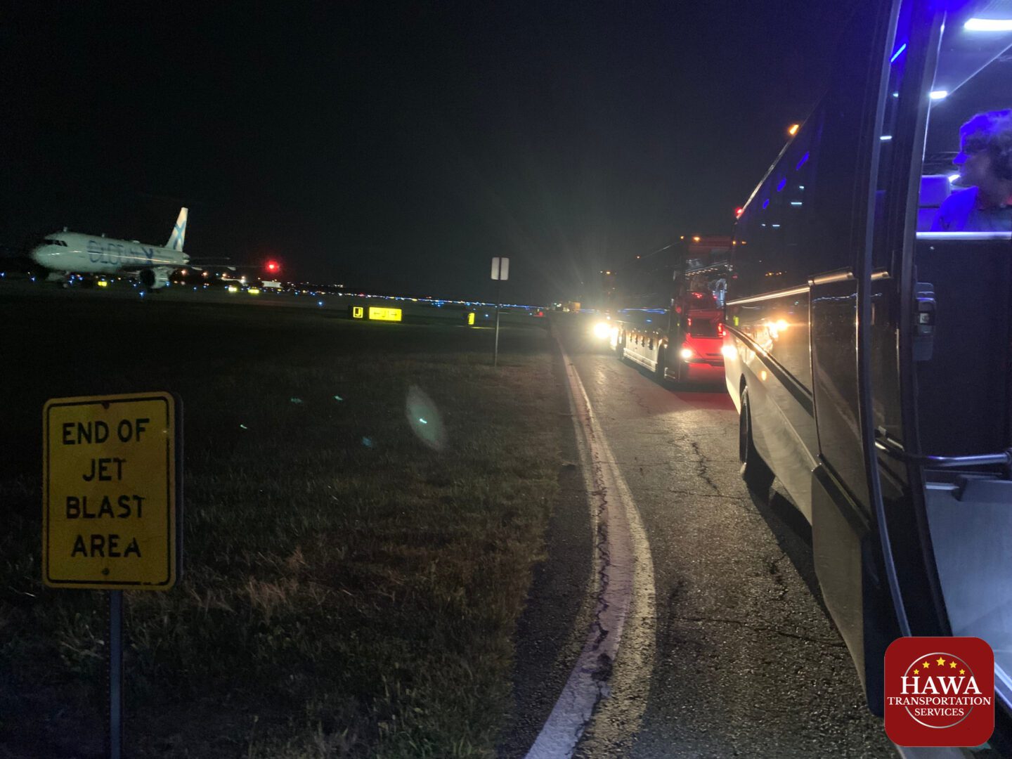 Nighttime coach near taxiing airplane and sign