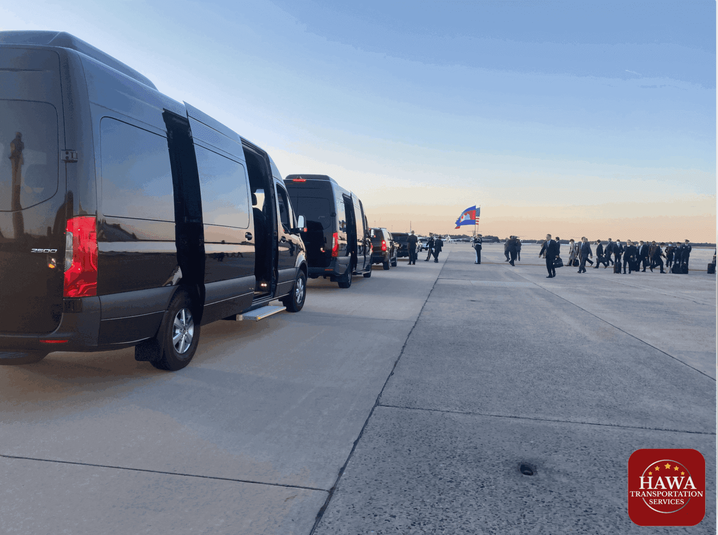 A group of people walking on the sidewalk near some black vans.